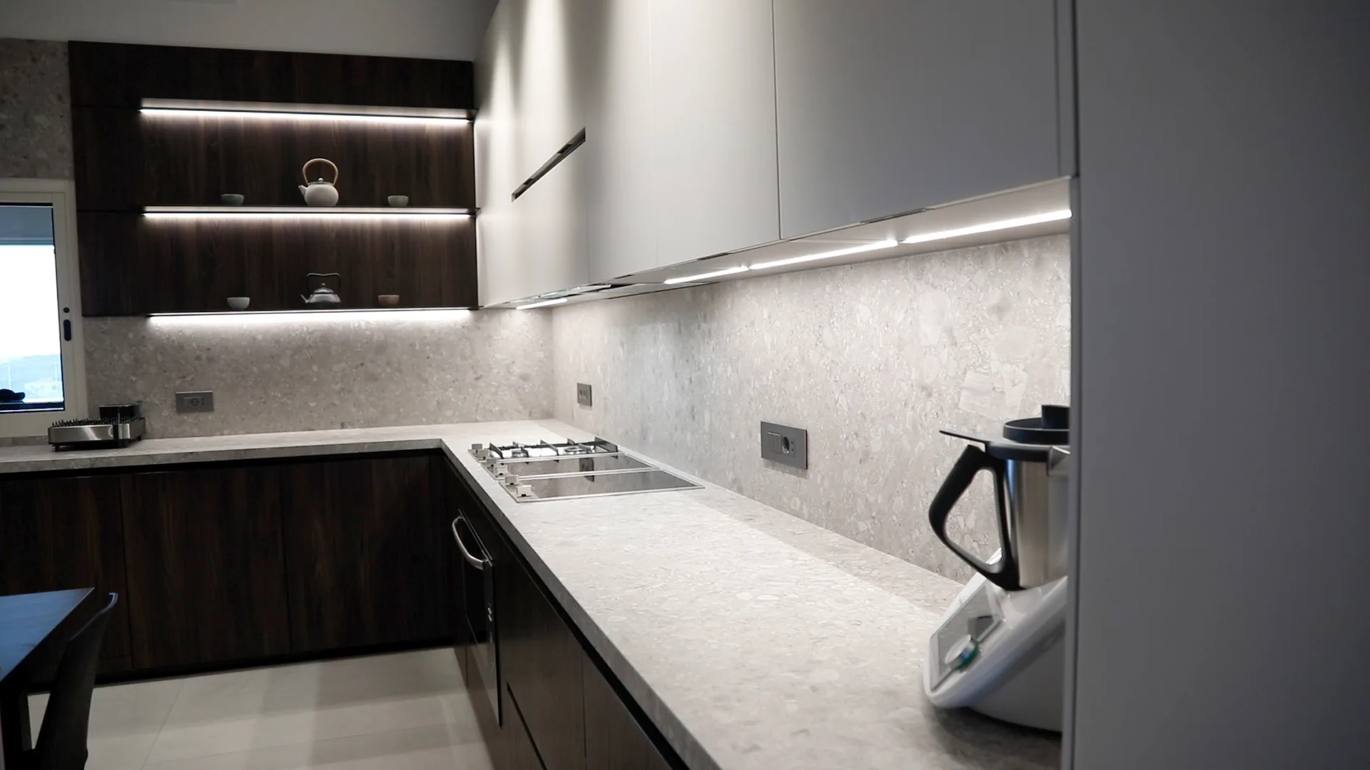 DV kitchen Dbayeh, Metn Lebanon — back-of-house prep kitchen / scullery with dark walnut base cabinetry, white handleless wall units, walnut LED-lit open shelving, terrazzo worktop and backsplash with integrated gas hob and undermount sink — KITWOOD Lebanon completed project