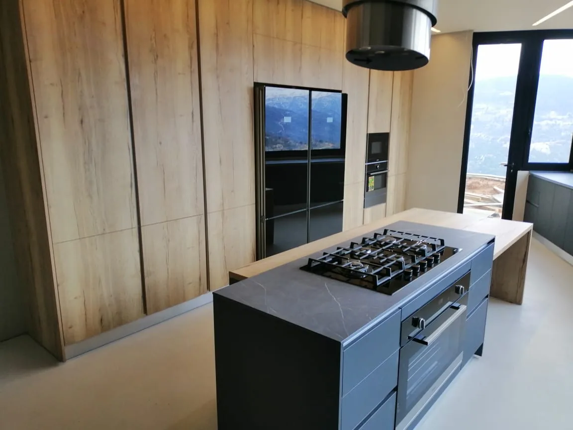 FQ kitchen executed in Faqra, Kesrwan — full-height light oak handleless cabinetry with charcoal stone island and mountain views — KITWOOD completed project