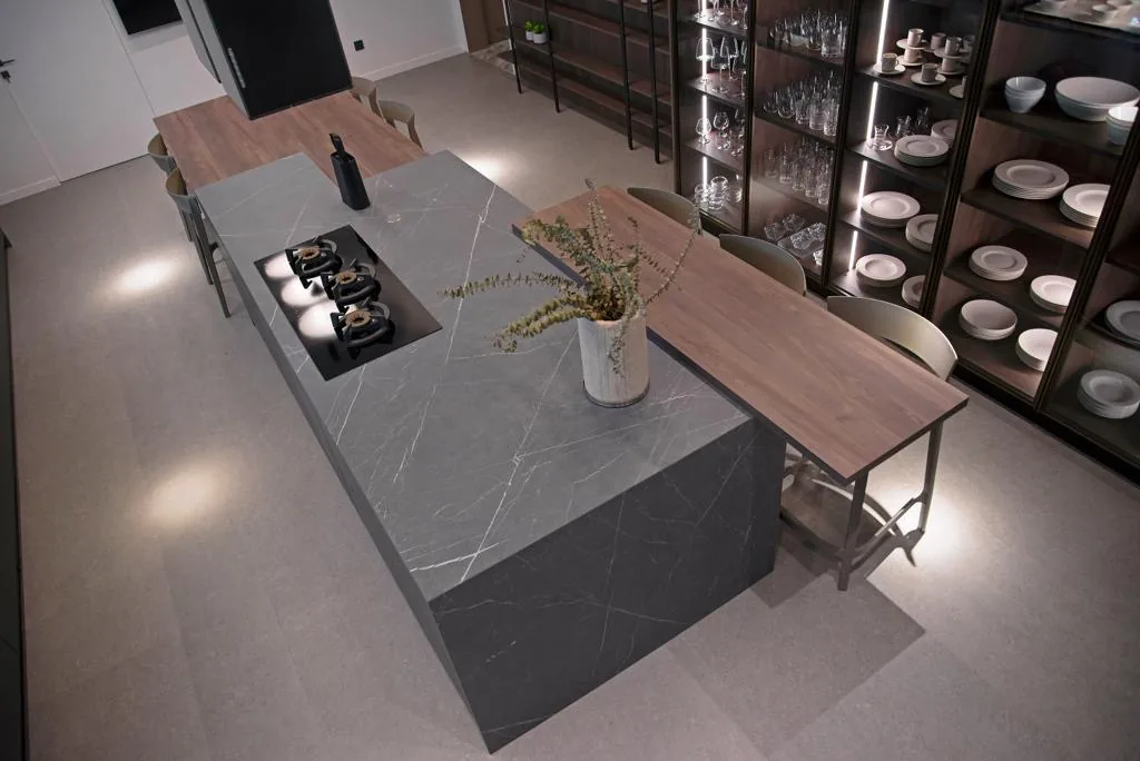 YK kitchen Yarze, Baabda Lebanon — overhead perspective of Pietra Grey marble waterfall island with extended walnut dining counter, integrated triple gas wok burner and bronze-frame walnut and glass display wall with LED-lit shelving for stemware and dinnerware — KITWOOD Lebanon completed project